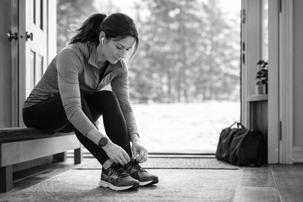 Middle-aged woman tying her running shoes by the door, representing momentum, daily movement, and consistent strength after 45